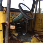 A yellow truck with a steering wheel and some rust.