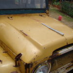 A close up of the hood on an old yellow truck.