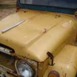 A close up of the hood on an old yellow truck.