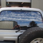 A truck with its rear window open and the reflection of clouds in it.